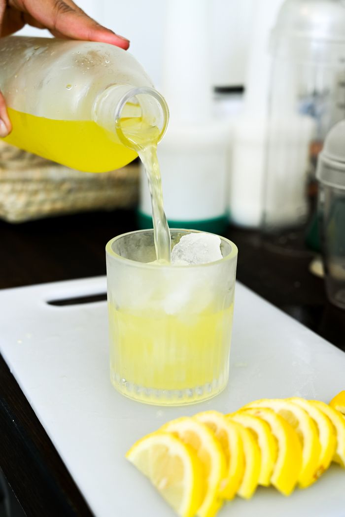 About Hand pouring refreshing lemon juice into a glass on a kitchen countertop, perfect summer drink.