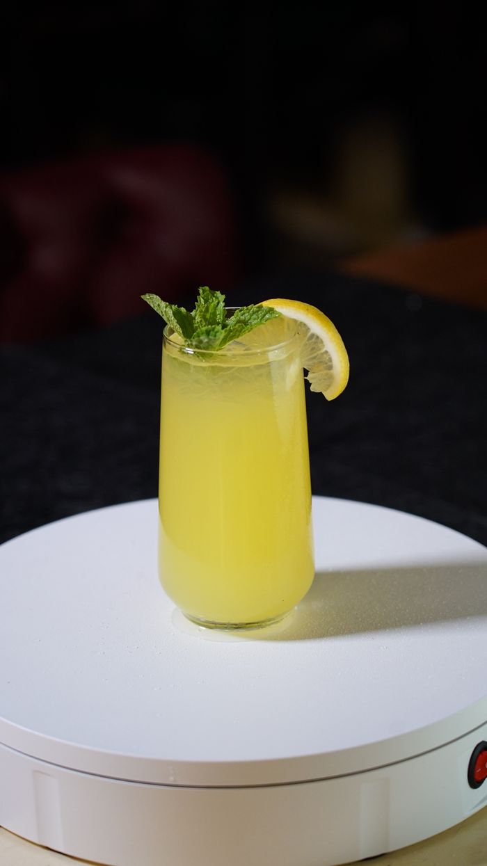 Home Tall glass of lemon mint drink garnished with lemon and mint on white surface.