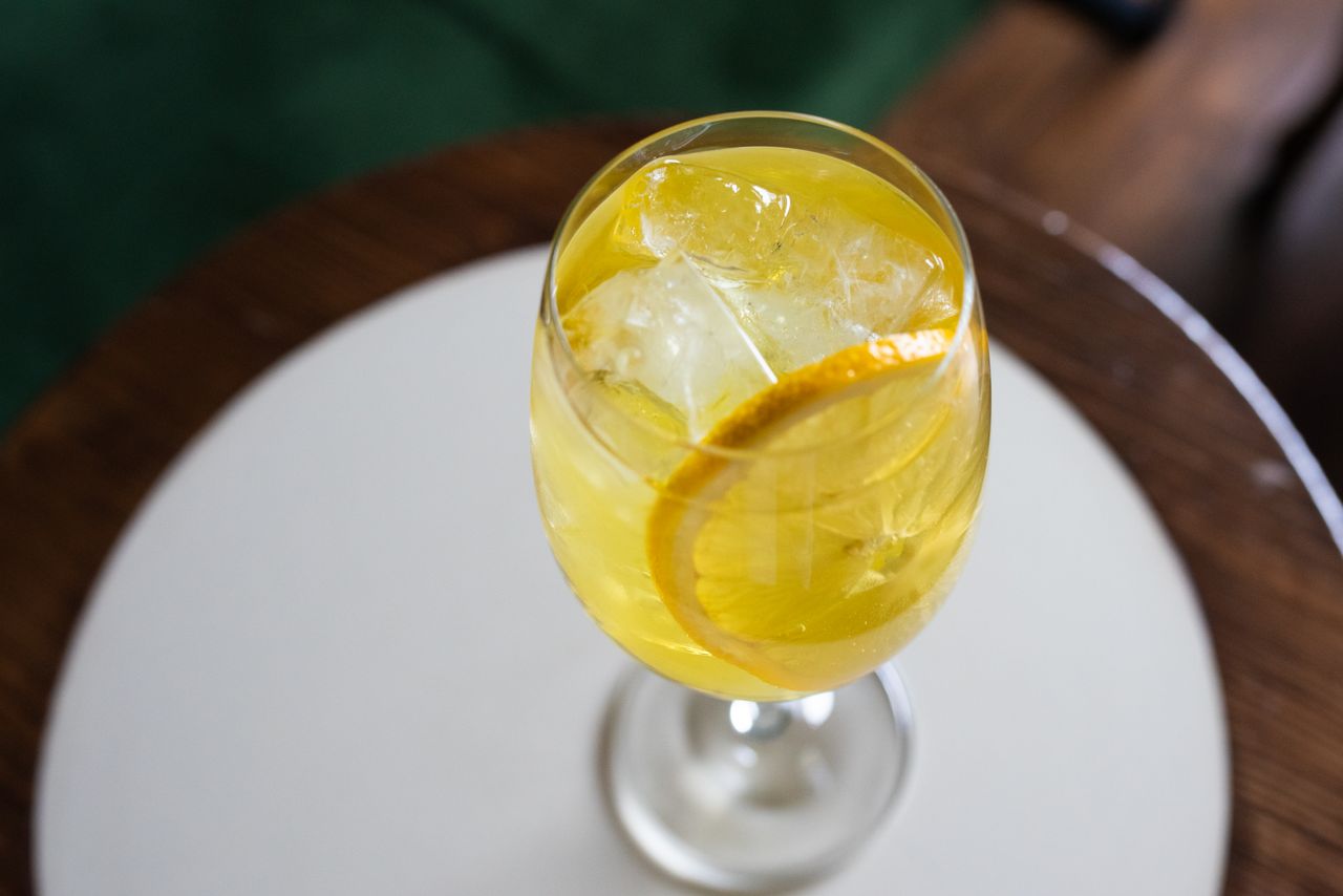 Services A top-down view of a refreshing citrus cocktail in a glass with ice and a lemon slice.