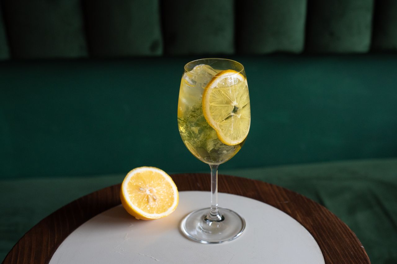 Home A citrusy lemon cocktail with ice in a wine glass on a wooden table, perfect for a refreshing drink.